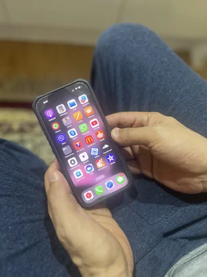 Un iPhone tenu en main, montrant l'écran d'accueil avec des applications sur fond de jean.