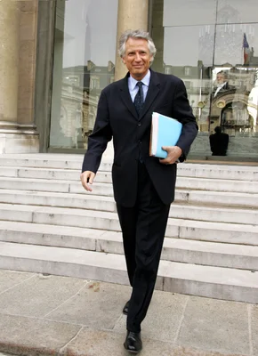Dominique de Villepin descendant des marches, dossier bleu sous le bras.