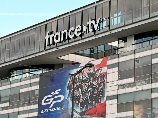 Bâtiment de France Télévisions avec une bannière promotionnelle pour 'GP Explorer', illustrant la programmation malgré les restrictions budgétaires.