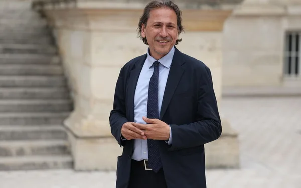 Jérôme Guedj souriant devant un bâtiment en pierre.