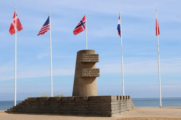 Monument commémoratif du Débarquement sur une plage normande, entouré des drapeaux des nations alliées.