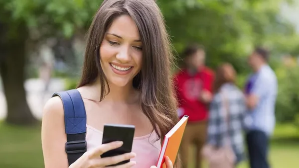 Une étudiante consulte son smartphone dans un parc, illustrant l'usage intensif d'Internet chez les jeunes.