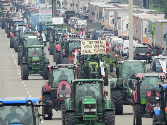 Manifestation d'agriculteurs alsaciens : un convoi de tracteurs bloque une autoroute avec la pancarte 'Demain nous voulons encore exister'.