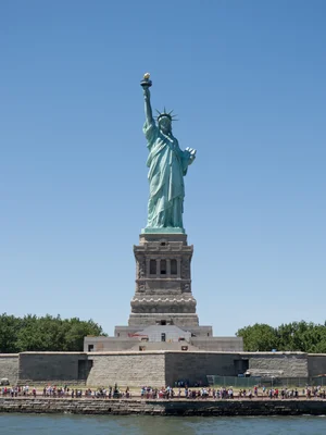 La statue de la Liberté sur son piédestal, avec des touristes au premier plan et un ciel bleu.