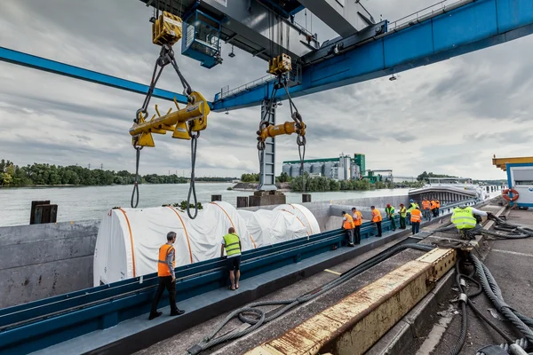 Déchargement de cargaison sur une barge à l'aide d'un portique, sur un fleuve par temps couvert.