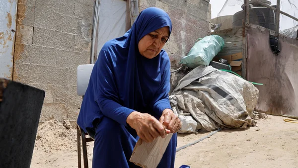Femme palestinienne âgée travaillant à l'extérieur dans un environnement précaire, illustrant la vie des civils à Gaza.