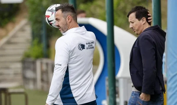 Joueur de l'OM en stage estival, jonglant avec le ballon sur un terrain, arborant une veste 'SUBLIME COTE D'IVOIRE'.