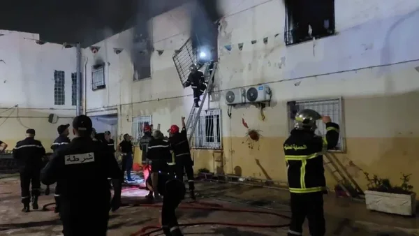 Pompiers et policiers intervenant de nuit pour éteindre un incendie dans un foyer d'accueil en Algérie.