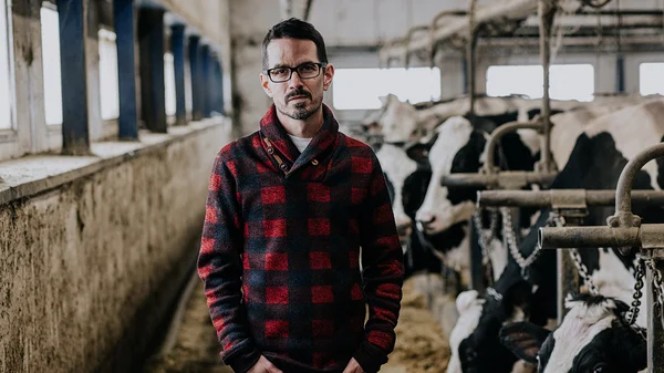Steve Poutré dans une étable, entouré de vaches laitières, illustrant l'univers de son roman « Lait cru ».