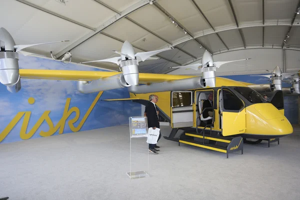 Le taxi volant électrique Wisk exposé en intérieur, des visiteurs l'examinant.