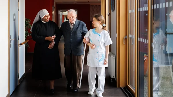 Un résident accompagné par une soignante et une religieuse des Petites Sœurs des Pauvres.