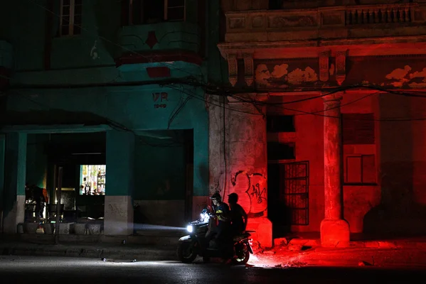 Scène nocturne à Cuba avec une moto éclairée entre des bâtiments colorés.