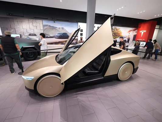 Un Tesla Roadster doré exposé dans un showroom, avec un Cybertruck visible en arrière-plan.