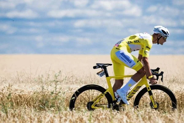 Un coureur en maillot jaune du Tour de France traverse un champ de blé sous un ciel bleu.