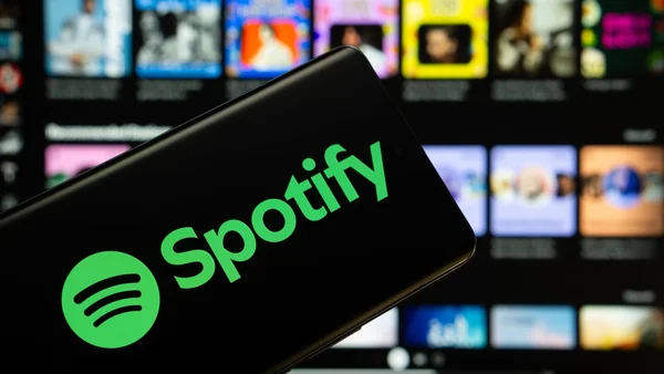 Smartphone avec logo Spotify devant une grille floue de pochettes d'albums.