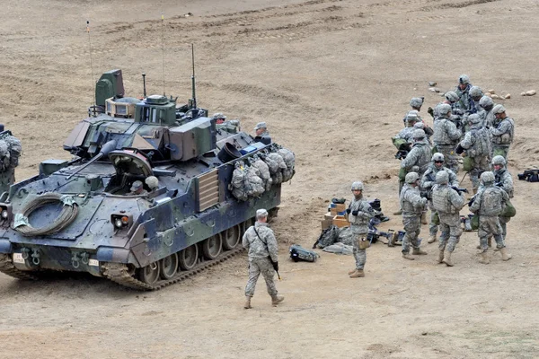 Soldats américains lors d'un exercice d'entraînement en tenue de camouflage près d'un véhicule blindé.