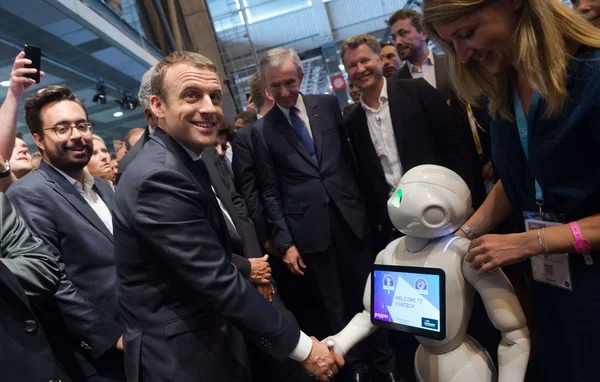Poignée de main entre un visiteur et un robot humanoïde lors du salon VivaTech, sous le regard d'une accompagnatrice et de participants souriants.