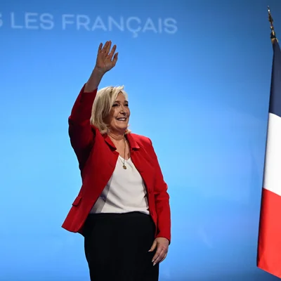Marine Le Pen saluant la foule devant un décor aux couleurs nationales.