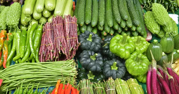 Étal de légumes variés sur un marché, mettant en avant haricots verts et courgettes.