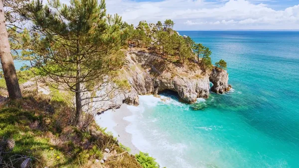 Plage de galets et falaises calcaires de Belle-Île-en-Mer, avec ses arches naturelles et ses pins.