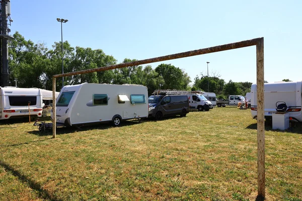 Campement de caravanes sur un terrain herbeux, avec un but de football rouillé au premier plan.