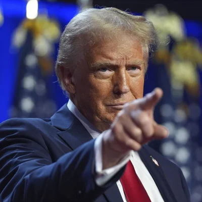 Donald Trump, doigt pointé, lors d'une prise de parole entouré de drapeaux américains.