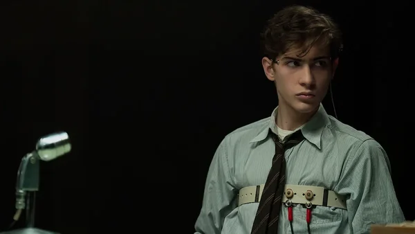 Jacob Tremblay dans le rôle du jeune Ted Kaczynski dans le film Unabomber de Netflix, vêtu d'une chemise et d'une cravate avec un équipement technique.