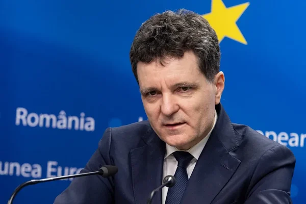 Un responsable roumain s'adressant à la presse, avec le logo 'România' et l'étoile européenne en arrière-plan.