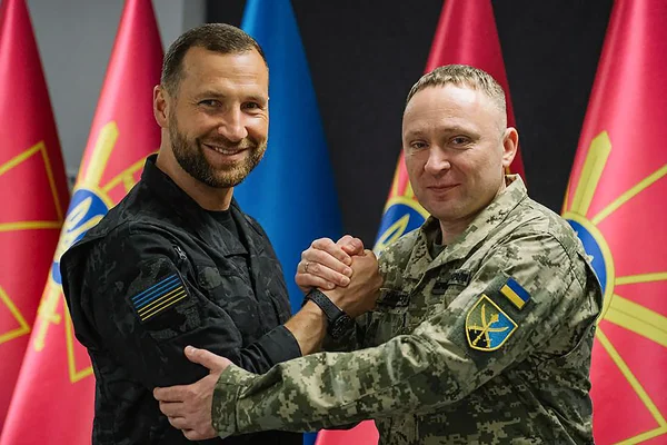 Mykhaïlo Drapaty et Oleksandr Syrskyi échangeant une poignée de main devant des drapeaux ukrainiens