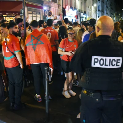 Rassemblement de supporters marocains dans une rue la nuit, avec un policier visible.