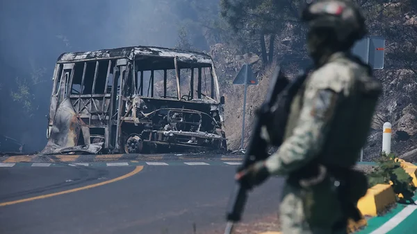 Un soldat mexicain surveille un bus calciné après une attaque, illustrant la violence des cartels.