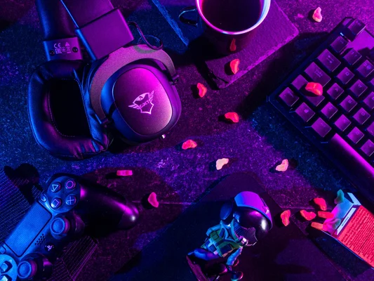 Setup de jeu vidéo avec casque, manette et clavier illuminés par des lumières néon, et bonbons sur le bureau.