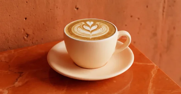 Un flat white avec un cœur en latte art, présenté sur une soucoupe en marbre.