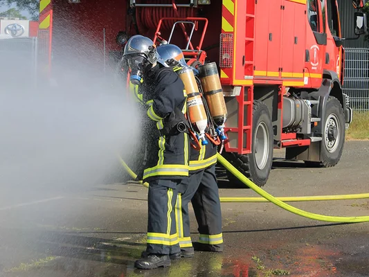 Exercice de lutte contre l'incendie : deux pompiers en action avec une lance à incendie.