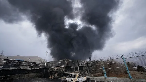 Fumée épaisse s'élevant d'un site touché aux Émirats, avec des véhicules détruits au premier plan.