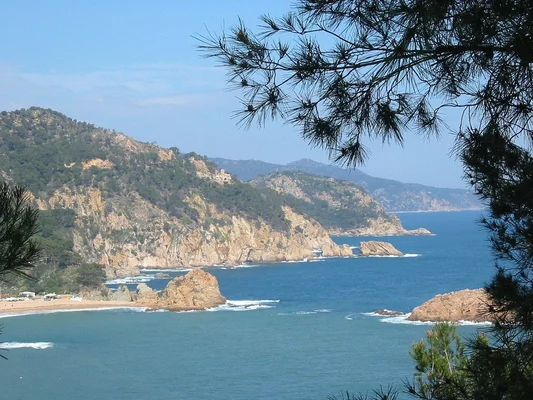Paysage côtier de la Costa Brava avec une plage de sable et des falaises rocheuses.