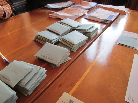 Dépouillement dans un bureau de vote en France : des enveloppes officielles de la République Française sont triées sur une table en bois.