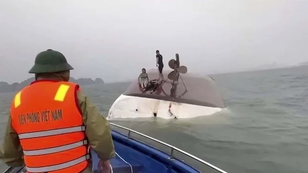 Un sauveteur observe deux personnes sur la coque retournée d'un bateau touristique chaviré au Vietnam.