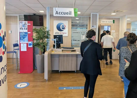Intérieur d'une agence Pôle emploi avec une file de demandeurs d'emploi.
