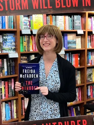 Une lectrice présentant le roman 'The Intruder' de Freida McFadden en librairie.