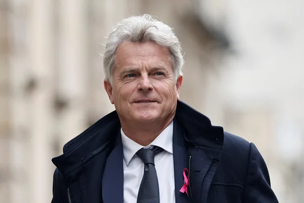 Fabien Roussel en extérieur, un ruban rose au revers.