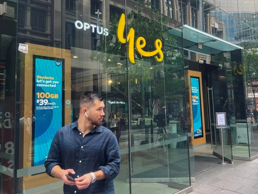 Un piéton devant une boutique Optus à Sydney, illustrant l'impact de la panne sur les clients.