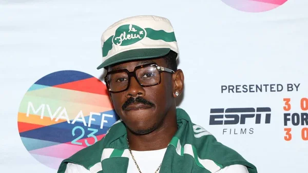 Tyler, The Creator lors d'un événement, arborant une casquette et une écharpe aux couleurs de sa marque Le Fleur.