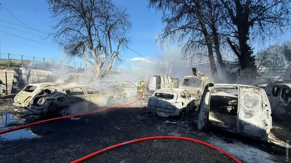 Intervention des pompiers sur des véhicules brûlés après un incendie dans un garage automobile.