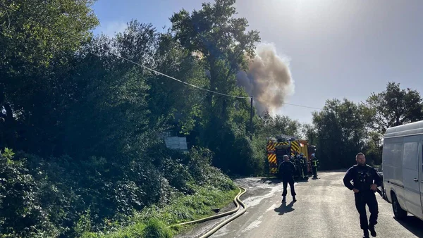 Les pompiers interviennent sur une route rurale près de Nantes alors qu'un panache de fumée s'élève des arbres lors de l'incendie d'un bidonville.