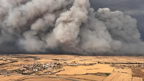 Un immense mur de fumée et de poussière plane au-dessus d'un paysage rural avec des champs agricoles et un petit village.