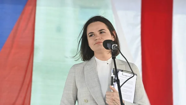 Svetlana Tsikhanovskaïa prenant la parole à un pupitre, entourée de drapeaux.