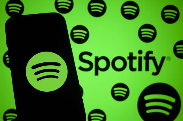 Smartphone avec le logo Spotify devant un fond vert décoré de motifs répétés de la marque.