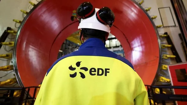 Un employé d'EDF en tenue de sécurité devant une structure industrielle circulaire rouge.