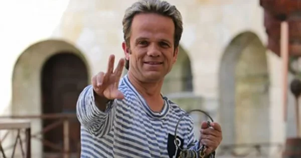 André Bouchet (Passe-Partout) en tenue décontractée, souriant devant un bâtiment.